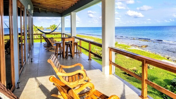 A covered outdoor seating area with wooden furniture and a view of the ocean.