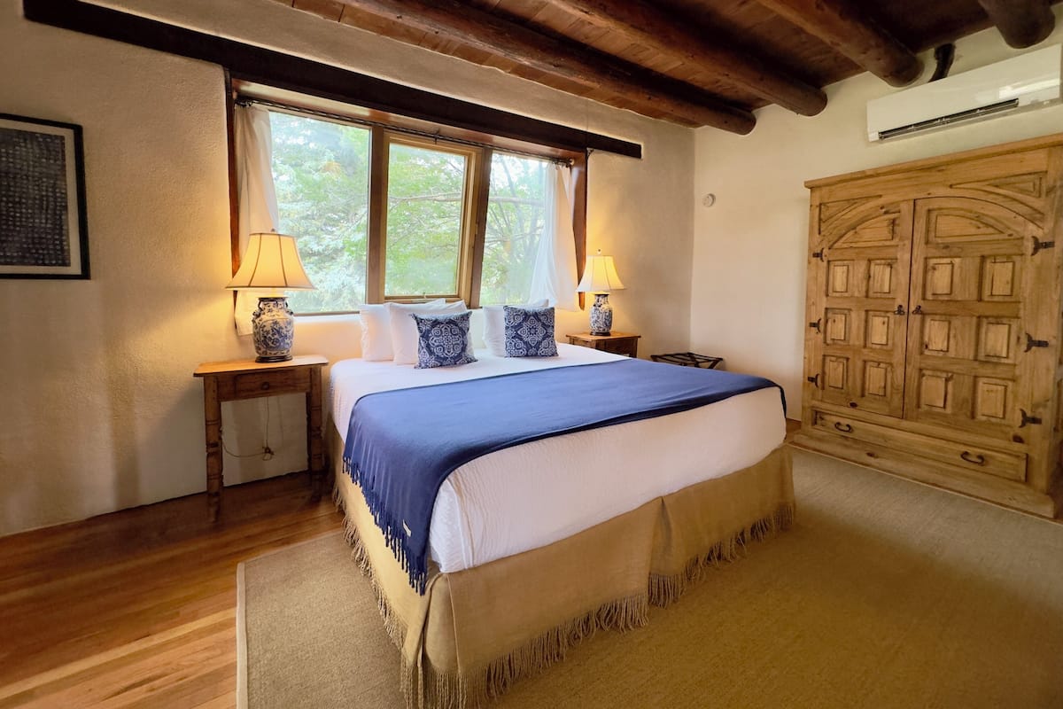 Een slaapkamer met een groot bed, twee nachtkastjes met lampen, een houten garderobe en een raam met gordijnen.