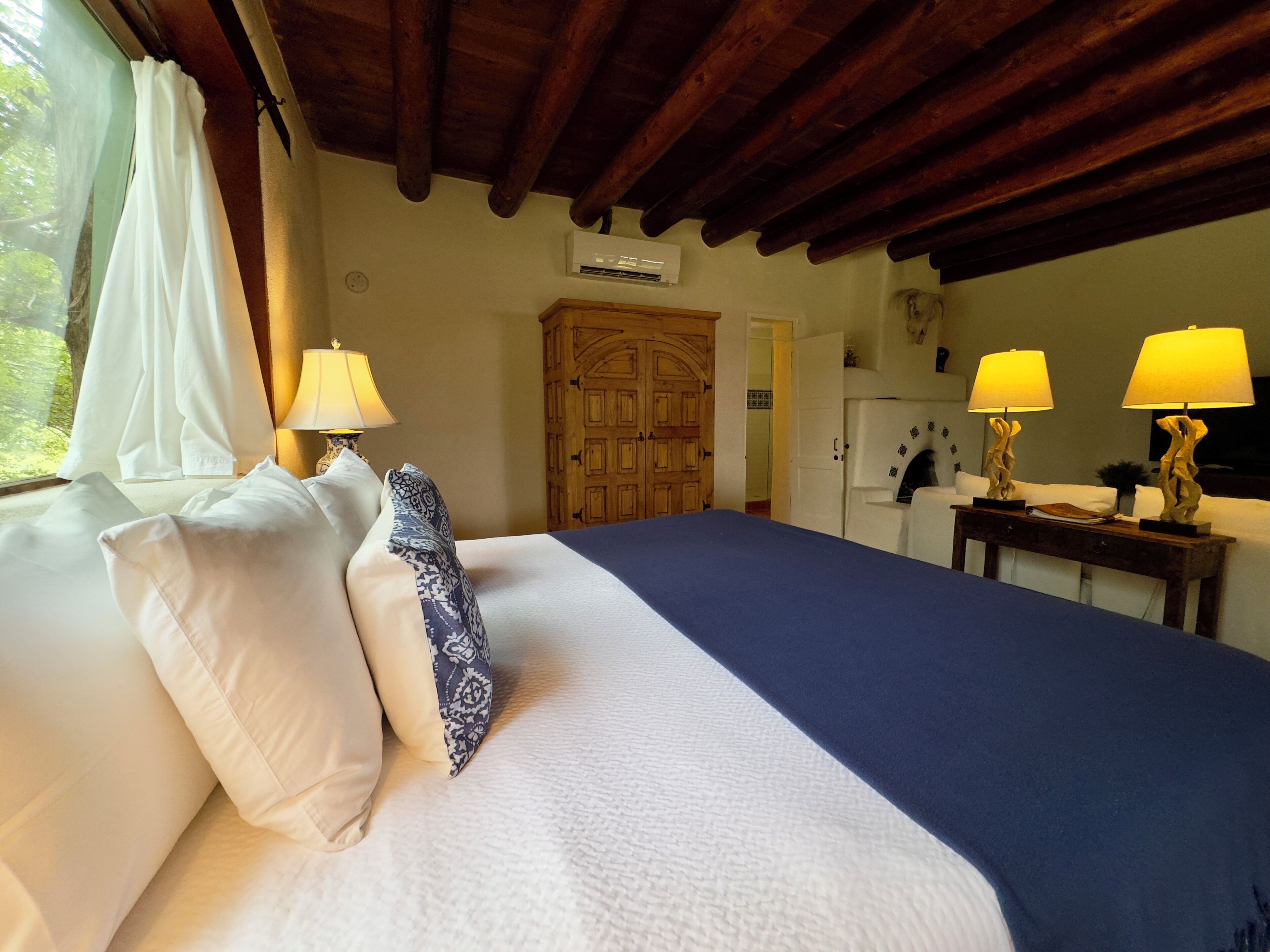 Un dormitorio con una cama grande, dos lámparas de noche, un armario de madera y vistas al exterior a través de una ventana.