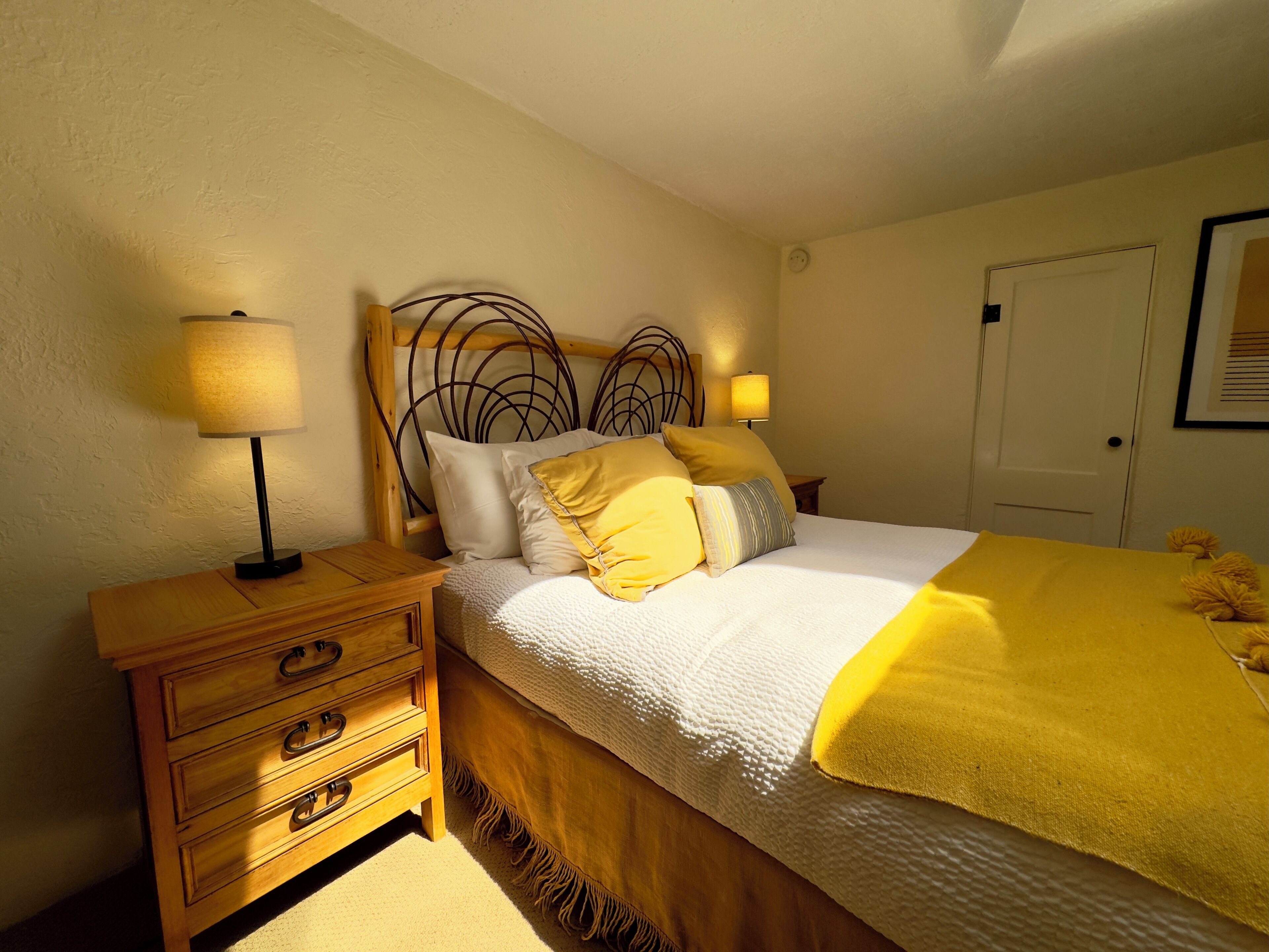 Ein Schlafzimmer mit einem Bett, einem Nachttisch aus Holz, zwei Nachttischlampen und einer Tür.