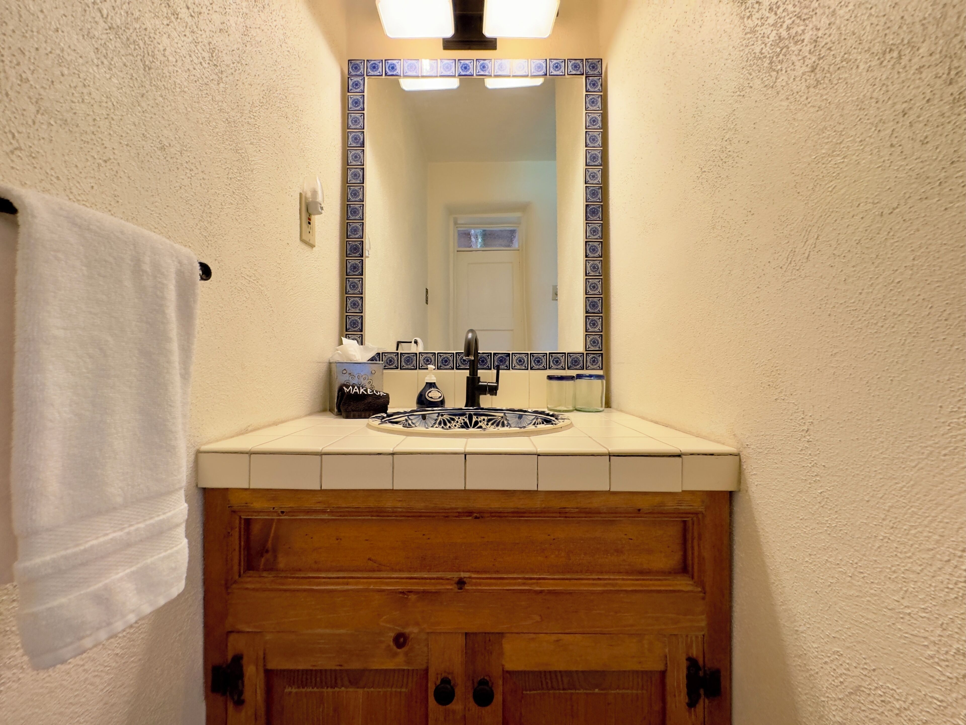 A bathroom with a white sink, a mirror with blue decorative tiles, and a wooden vanity.