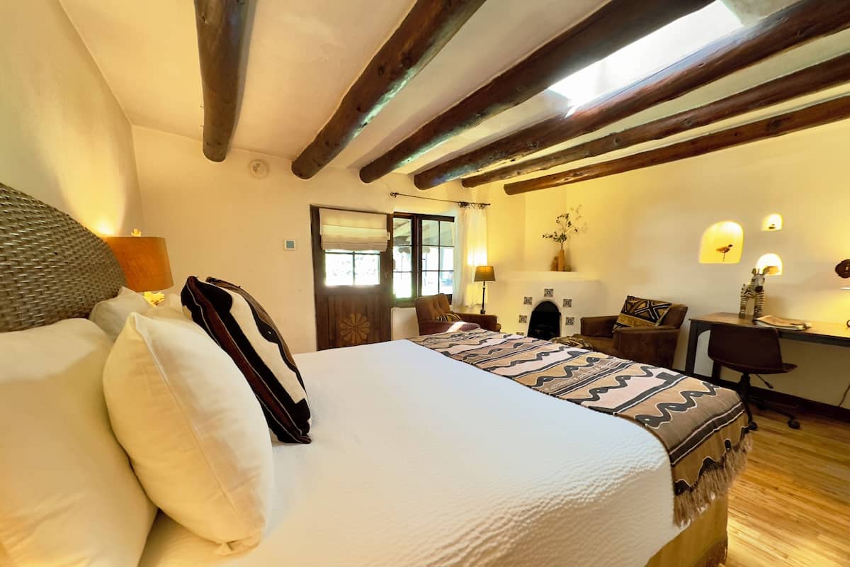Een slaapkamer met een groot bed, houten balken, een bureau en een open haard.
