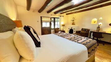 A bedroom with a large bed, wooden beams, a desk, and a fireplace.