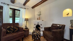 Un salon chaleureux avec deux canapés marron, une petite table ronde avec une lampe, une cheminée ornée de carreaux décoratifs et une fenêtre avec des rideaux.