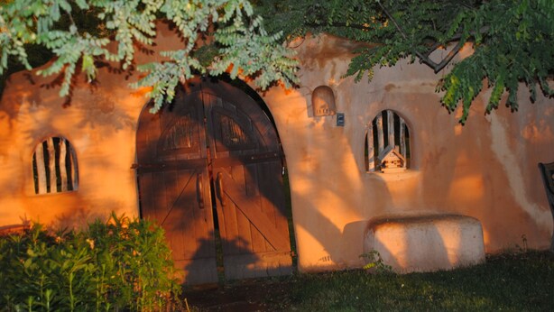 Un bâtiment rustique doté d’une grande porte en bois, de petites fenêtres et d’un banc en pierre.