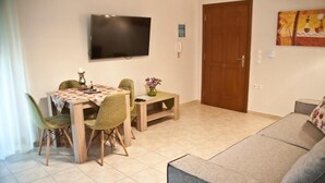 A living room with a sofa, a dining table with chairs, a TV mounted on the wall, and a door. - Chalkida Apartments (Chalcis)