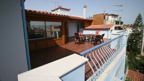 A balcony with a table and chairs, a view of the sea, and a building with a tiled roof. - Chalkida Apartments (Chalcis)