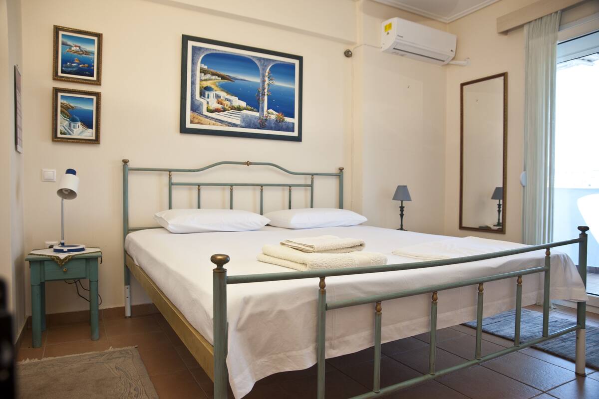 Un dormitorio con cama, mesita de noche, lámpara, un cuadro y una ventana con cortinas.