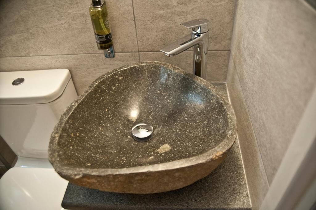 A bathroom with a stone sink, a toilet, and a shower area.