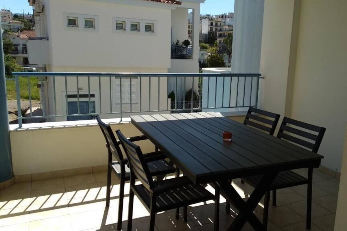 Un balcón con una mesa y sillas, una taza roja sobre la mesa, y vista de edificios al fondo.