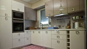 A modern kitchen with white cabinets, stainless steel appliances, and a tiled backsplash. - Chalkida Apartments (Chalcis)