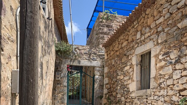 A stone staircase leading to a gated entrance in a narrow alleyway with stone walls and a blue tarp overhead. - Nomitsi Traditional House (West Mani)