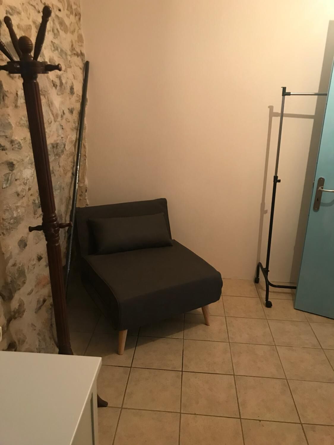 Ein kleines, dunkel gefärbtes Sofa steht in einer Ecke des Raumes mit Fliesenboden und Steinwand.