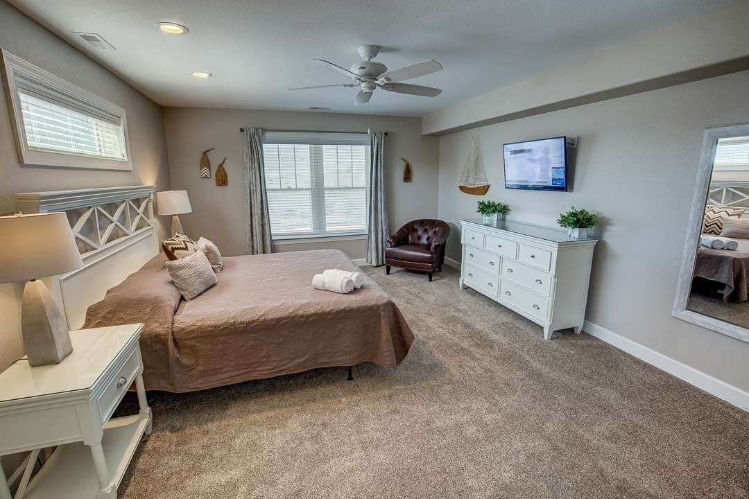 A bedroom with a bed, a desk, a chair, a dresser, a television, and a ceiling fan.