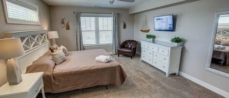 A bedroom with a bed, a desk, a chair, a dresser, a television, and a ceiling fan.