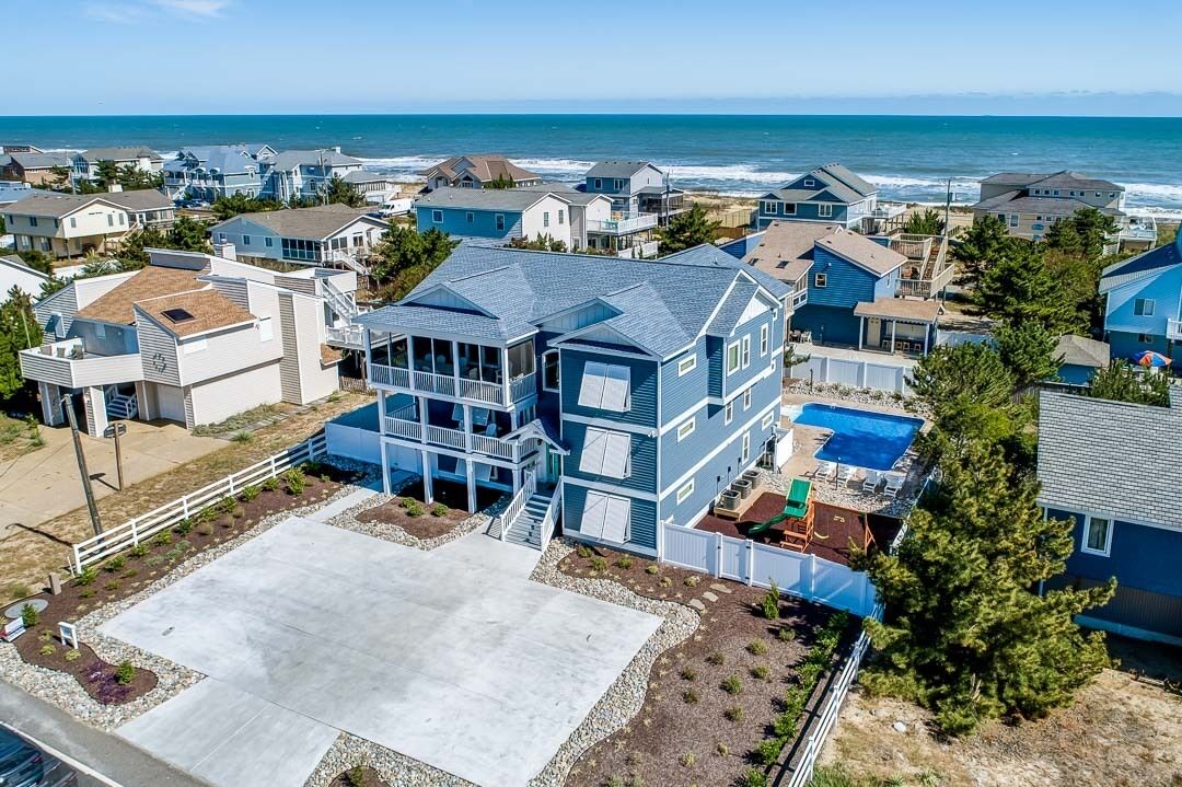 A coastal residential area with houses, a large blue house with a balcony, and a view of the ocean.