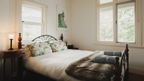 A bedroom with a bed, two bedside tables, a lamp, and two windows. - White Rose Cottage Healesville (Healesville)