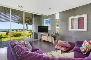 A modern living room with a large TV, purple sofas, and a view of the outdoors.
