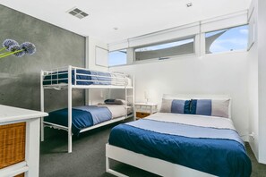 A room with bunk beds, a desk, a nightstand, and a window with a view.