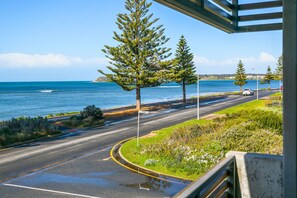 A coastal road with a clear view of the ocean, a road sign indicating 'Wood S', and a pedestrian pathway alongside the road.