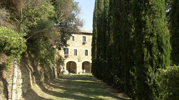 Un edificio de piedra con arcos, rodeado de altos árboles y un sendero estrecho.