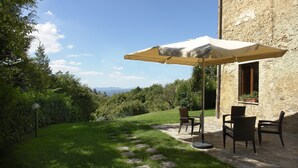 Un patio al aire libre con suelo de piedra, una mesa, sillas y un amplio paraguas que proporciona sombra.