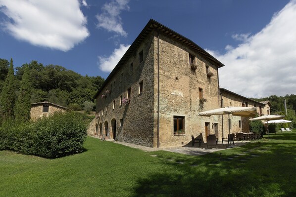 Un edificio de piedra con patio, mesas al aire libre y un pequeño jardín.
