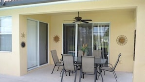 Une terrasse couverte avec une table et des chaises, un ventilateur de plafond et des éléments décoratifs sur les murs.