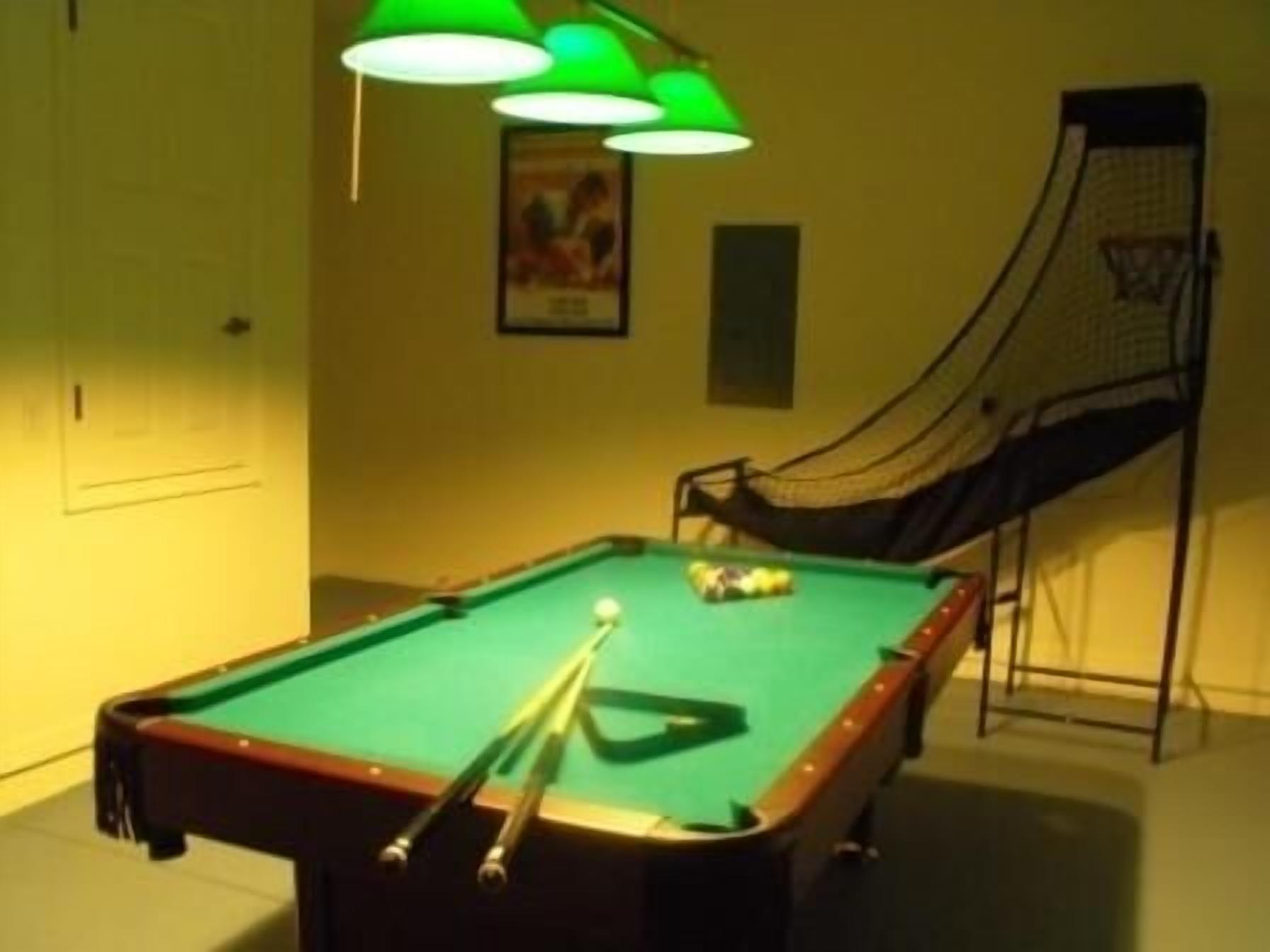 A pool table with a green felt surface, surrounded by a yellow wall with a framed picture.