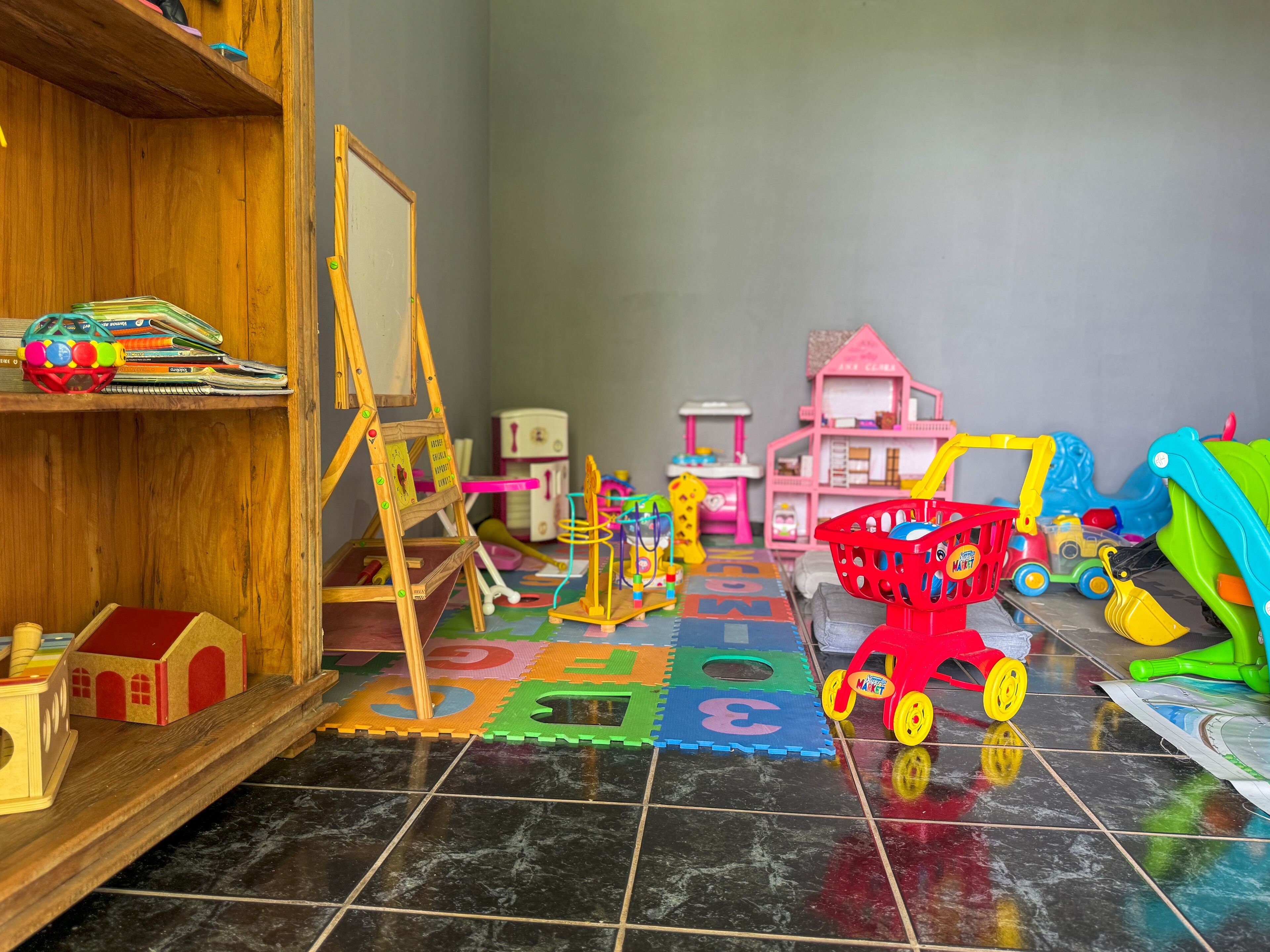 A playroom with a wooden shelf, a small easel, a toy house, and a toy car.
