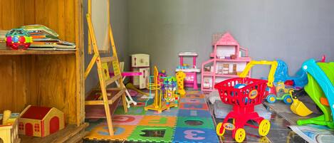 A playroom with a wooden shelf, a small easel, a toy house, and a toy car.