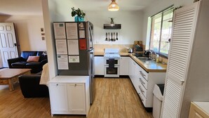 Une cuisine compacte équipée d’un réfrigérateur, d’une cuisinière et d’un évier. On y trouve une table à manger en bois et un canapé noir avec un coussin.