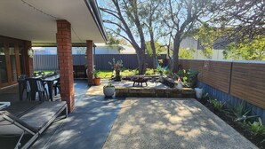 Une terrasse à l’arrière de la maison, avec un espace barbecue, un coin salon et un petit jardin.