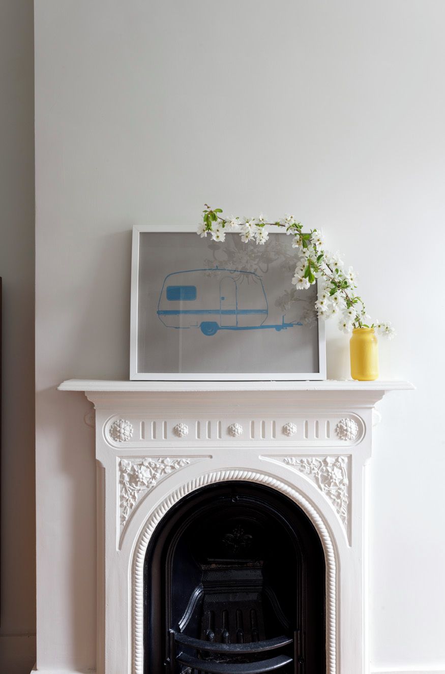 A white fireplace with a framed artwork of a blue van and white flowers.