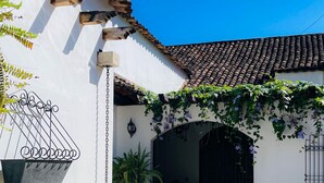 A courtyard with a swimming pool, lounge chairs, and a white building with a tiled roof.