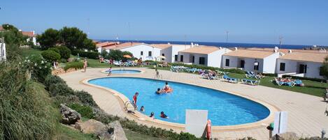A swimming pool surrounded by lounge chairs and a view of the sea.