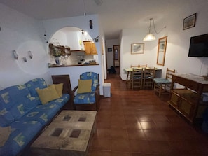 Uma sala de estar com sofá, duas poltronas, uma mesa de centro e um espaço de jantar com mesa e cadeiras.