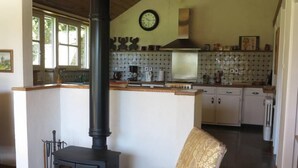 A cozy kitchen with a wood-burning stove, white cabinets, and a clock on the wall.