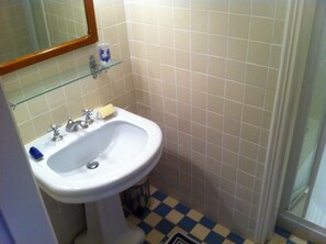 Un baño con un lavamanos blanco, un espejo y un estante de vidrio.