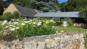 A stone building with a grey roof, surrounded by a garden with white flowers and green shrubs.