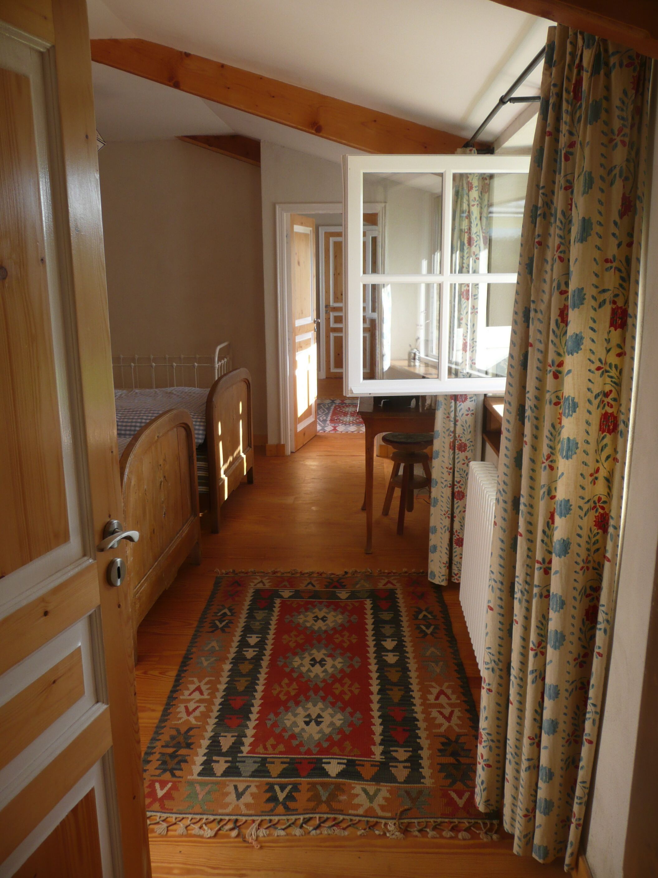 A room with a bed, a wooden chair, a small table, and a window with curtains.