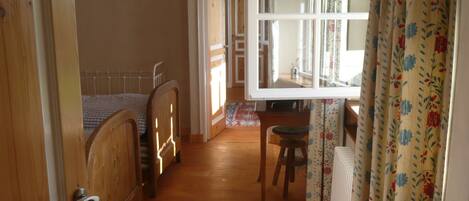 A room with a bed, a wooden chair, a small table, and a window with curtains.