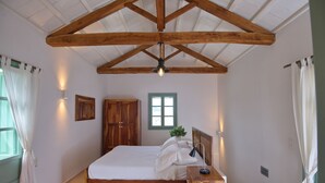 A bedroom with a wooden bed frame, a nightstand, a window with a view, and a ceiling with exposed beams.