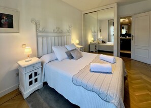 Ein ordentlich eingerichtetes Schlafzimmer mit einem großen Bett, Nachttischen mit Lampen, einem Spiegel und einem Kleiderschrank.