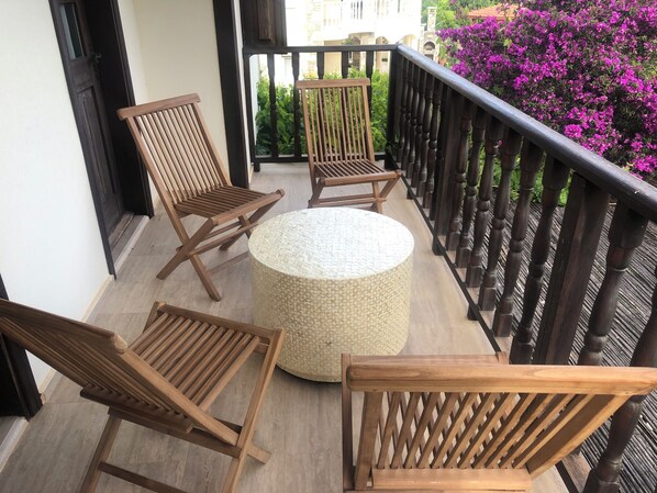 Un balcón con sillas de madera y una mesa redonda, rodeado por una barandilla de madera.