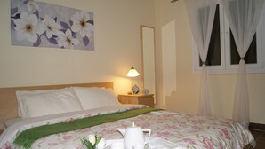 Ein ordentlich bezogenes Bett mit floraler Bettdecke, ein Nachttisch mit Lampe und ein Tablett mit Tee-Service.