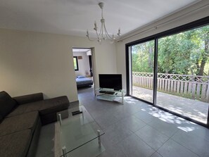 A modern living room with a glass coffee table, a sofa, a TV on a stand, and a large sliding glass door leading to a balcony with a wooden fence. - Quiet villa with heated pool, 10 minutes from Saint Cyprien beach (Porto-Vecchio)