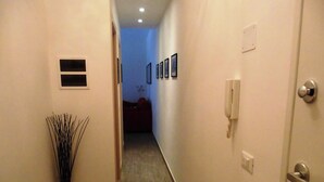 Un pasillo estrecho con suelo de madera, un teléfono en la pared y una puerta con pomo plateado.