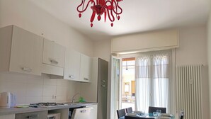 Una cocina moderna con gabinetes blancos, una estufa a gas y un lavavajillas. Hay un comedor con una mesa de vidrio y sillas, y una lámpara de araña roja.