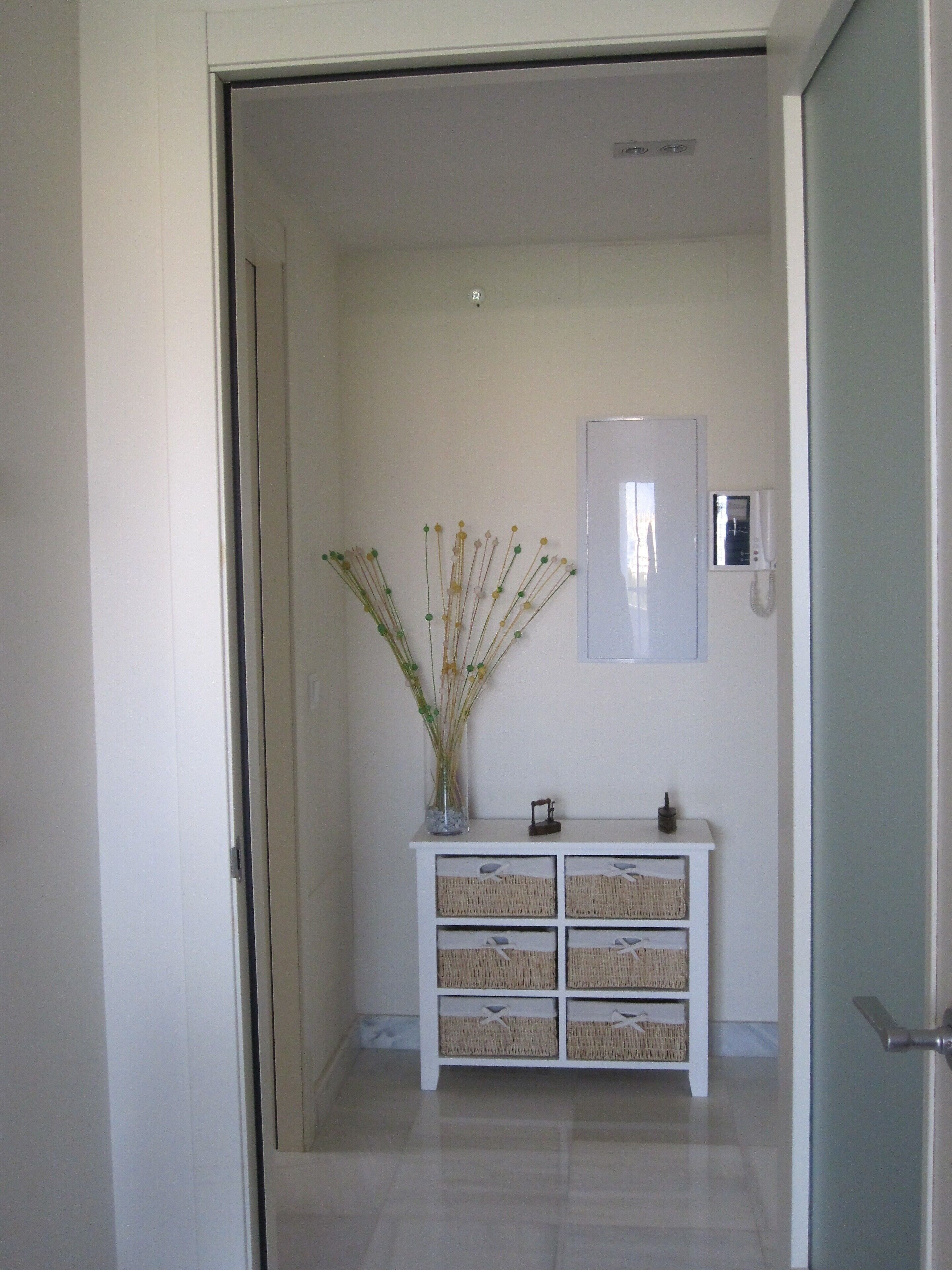 Un couloir avec une console blanche, des paniers en osier et un vase contenant des plantes séchées.